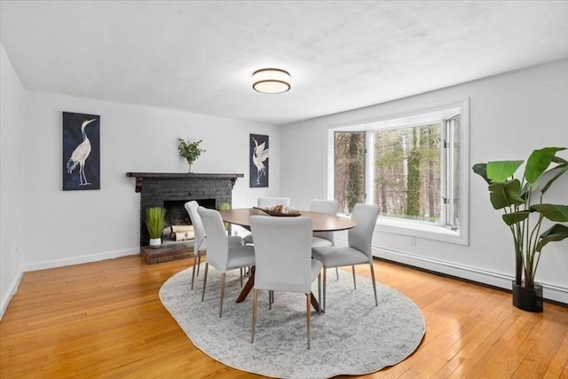 dining room with a brick fireplace, baseboards, and hardwood / wood-style flooring