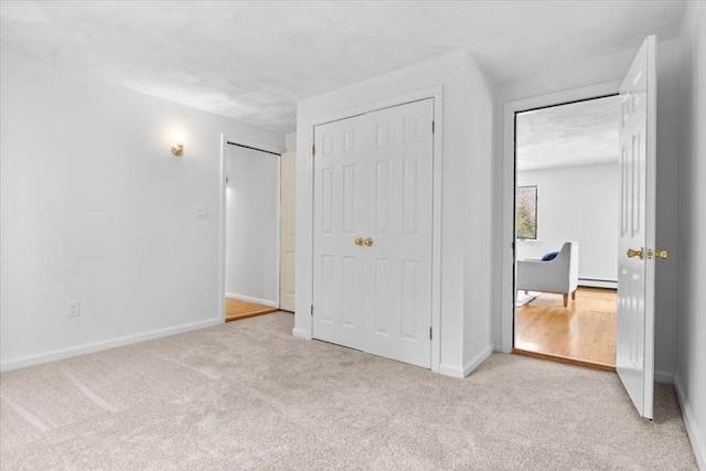 unfurnished bedroom with baseboards, a baseboard radiator, and light colored carpet