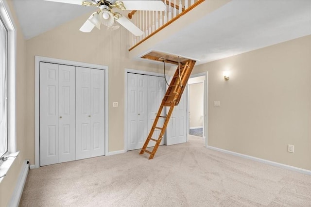 unfurnished bedroom featuring a baseboard heating unit, multiple closets, attic access, and light colored carpet