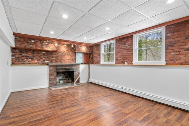 unfurnished living room with a baseboard heating unit, a drop ceiling, a fireplace, and wood finished floors