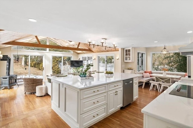 kitchen with white cabinets, dishwasher, a kitchen island, open floor plan, and a wood stove