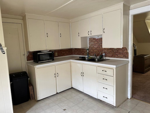 kitchen featuring a sink, stainless steel microwave, backsplash, light countertops, and white cabinets