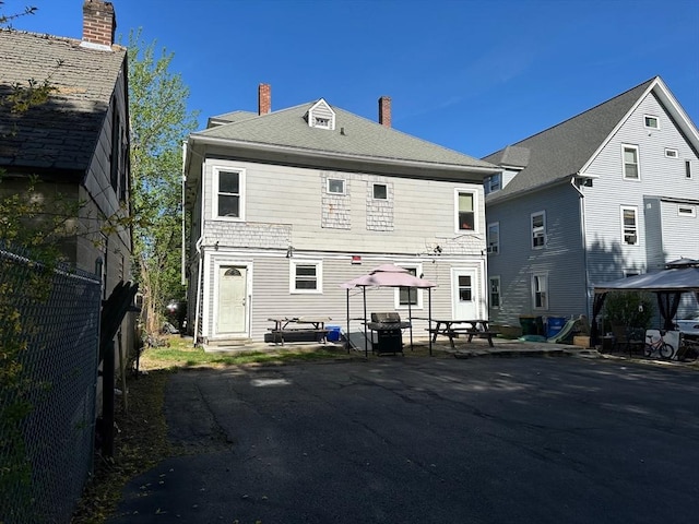 rear view of property featuring fence, a gazebo, a patio area, and a chimney