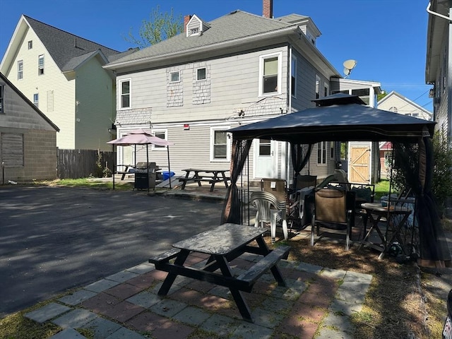 back of property featuring a gazebo, fence, a patio area, a chimney, and outdoor dining area