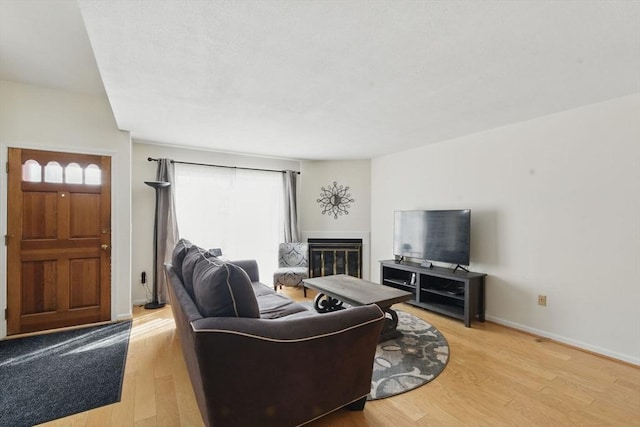 living area featuring a glass covered fireplace, light wood-style flooring, and baseboards