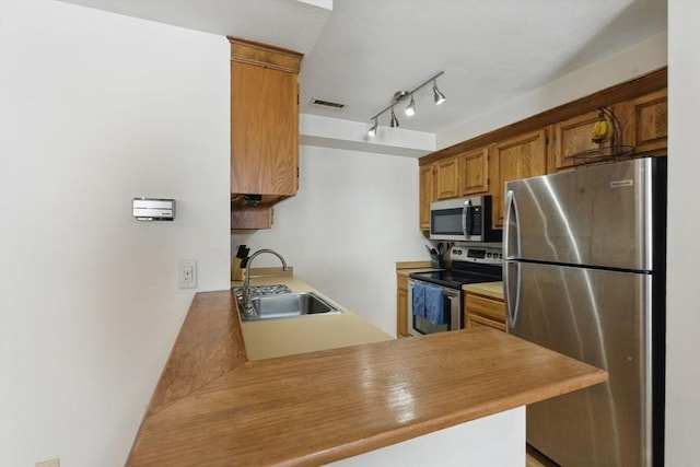 kitchen with brown cabinets, visible vents, appliances with stainless steel finishes, a sink, and a peninsula