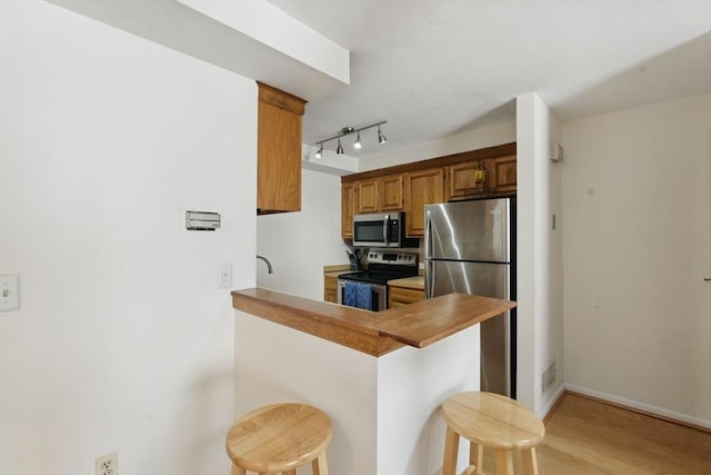 kitchen with a breakfast bar, light wood-style flooring, appliances with stainless steel finishes, brown cabinetry, and a peninsula