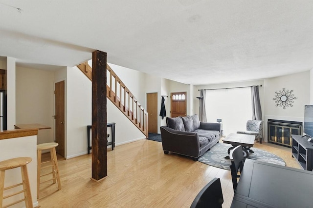 living room with light wood-style floors, a glass covered fireplace, stairway, and baseboards