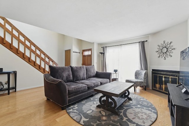 living room with stairway, a fireplace with flush hearth, light wood-style flooring, and baseboards