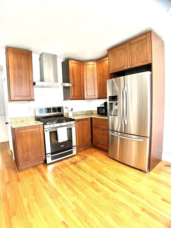 22-24 Ellison Ave Unit 1, Boston, MA 02126 - kitchen with appliances with stainless steel finishes, wall chimney exhaust hood, light wood-style flooring, brown cabinets, and light stone countertops