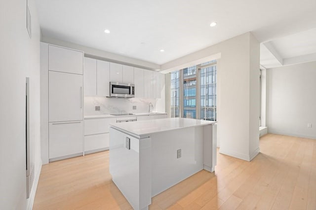 kitchen with black electric stovetop, light wood-style flooring, a center island, stainless steel microwave, and decorative backsplash