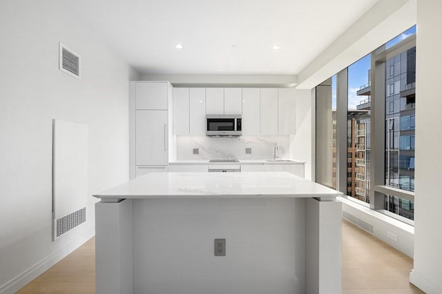 kitchen with white cabinets, stainless steel microwave, light wood-type flooring, and black electric stovetop