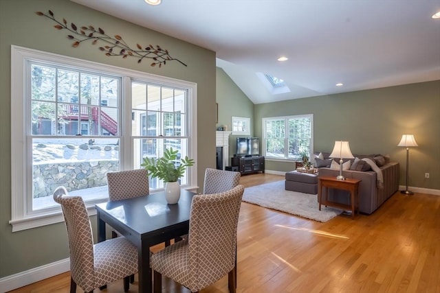 dining room featuring vaulted ceiling with skylight and light hardwood / wood-style floors