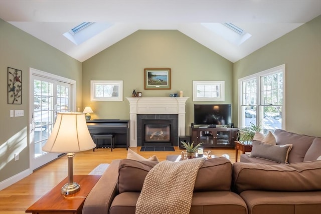 living room with a healthy amount of sunlight, lofted ceiling with skylight, a tile fireplace, and light hardwood / wood-style flooring