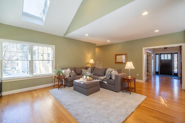 living room featuring lofted ceiling with skylight and light hardwood / wood-style floors