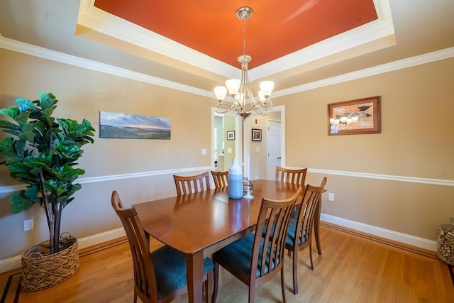 dining area featuring crown molding, a notable chandelier, a raised ceiling, and light wood-type flooring