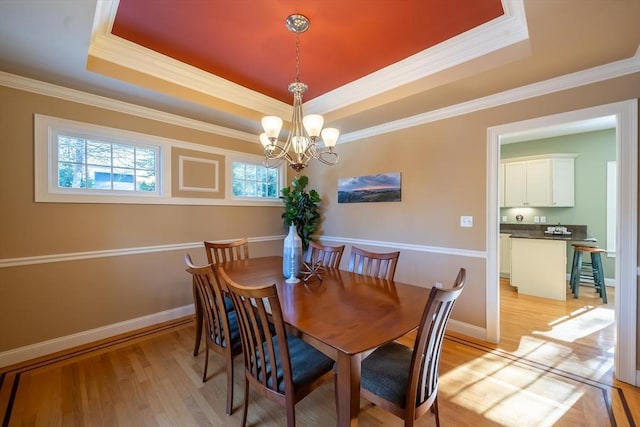 dining room with crown molding, a notable chandelier, a tray ceiling, and light wood-type flooring