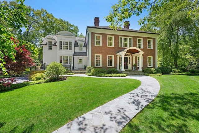 colonial home with brick siding, a chimney, and a front yard