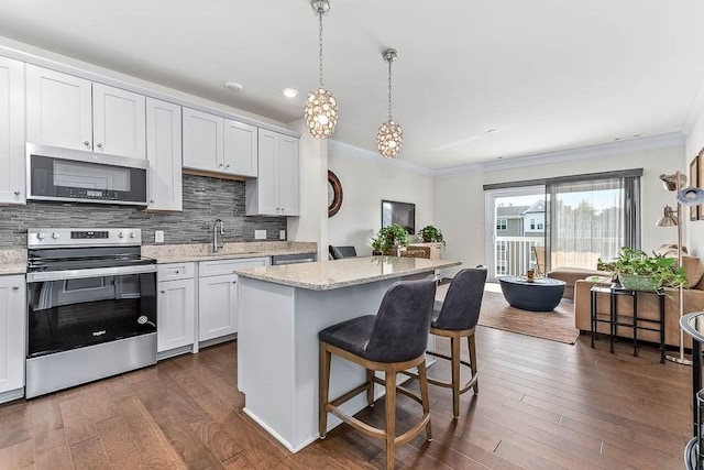 kitchen featuring stainless steel appliances, white cabinets, ornamental molding, a center island, and pendant lighting