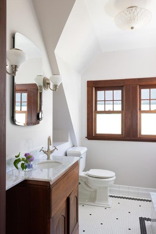 half bath featuring lofted ceiling, healthy amount of natural light, toilet, vanity, and tile patterned floors