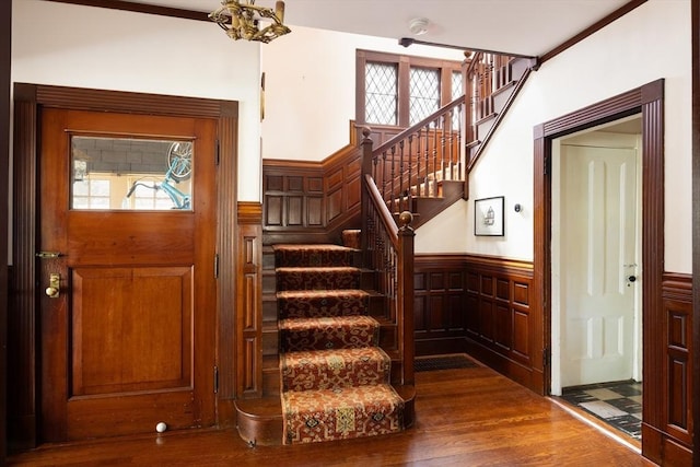 foyer entrance featuring wainscoting, dark wood-style floors, stairway, and a chandelier
