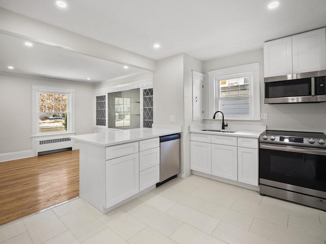 kitchen featuring sink, radiator heating unit, stainless steel appliances, white cabinets, and kitchen peninsula