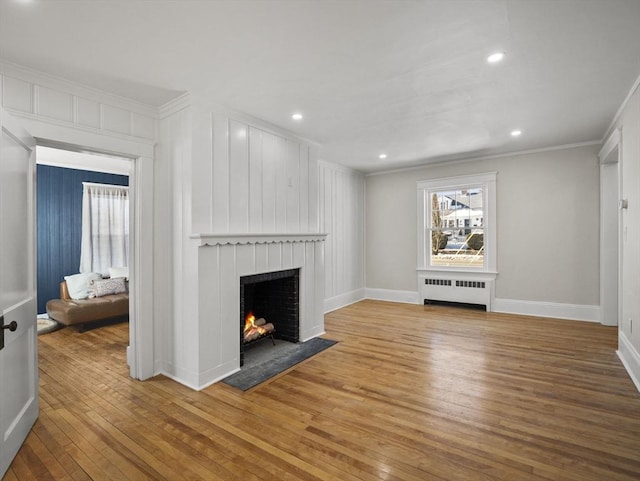 unfurnished living room with crown molding, radiator heating unit, and wood-type flooring