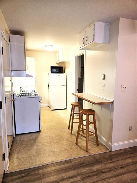 6 Venice St Unit F2, Danvers, MA 01923 - kitchen featuring white appliances, baseboards, white cabinetry, and a kitchen bar
