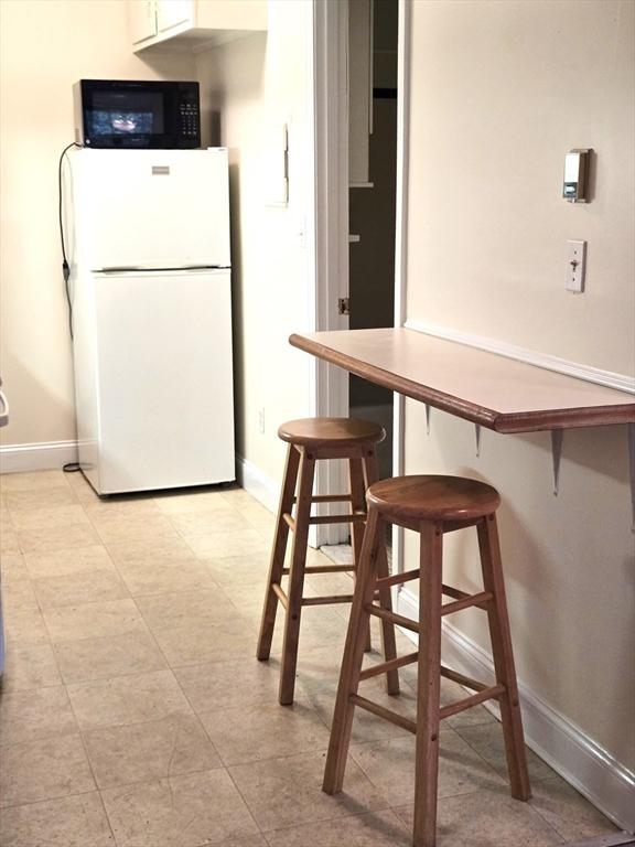 6 Venice St Unit F2, Danvers, MA 01923 - kitchen with freestanding refrigerator, black microwave, baseboards, a kitchen breakfast bar, and white cabinetry