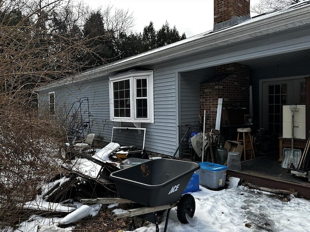 view of snowy exterior with brick siding and a chimney