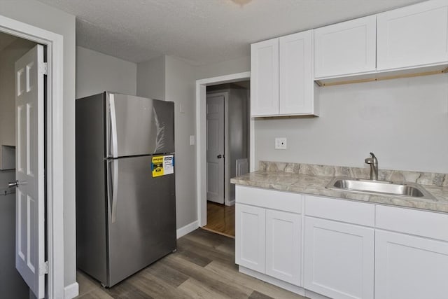 kitchen featuring freestanding refrigerator, wood finished floors, light countertops, white cabinetry, and a sink