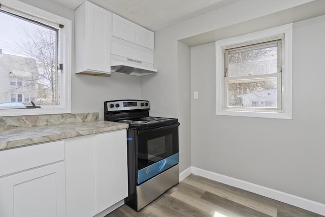 kitchen featuring baseboards, light countertops, stainless steel electric range, white cabinetry, and under cabinet range hood