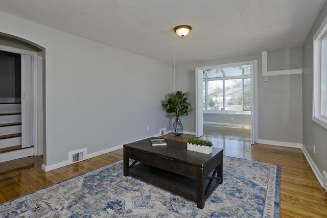 sitting room featuring visible vents, wood finished floors, baseboards, stairway, and arched walkways