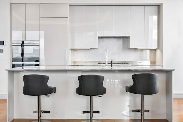 kitchen featuring light wood-type flooring, backsplash, light stone counters, and a breakfast bar