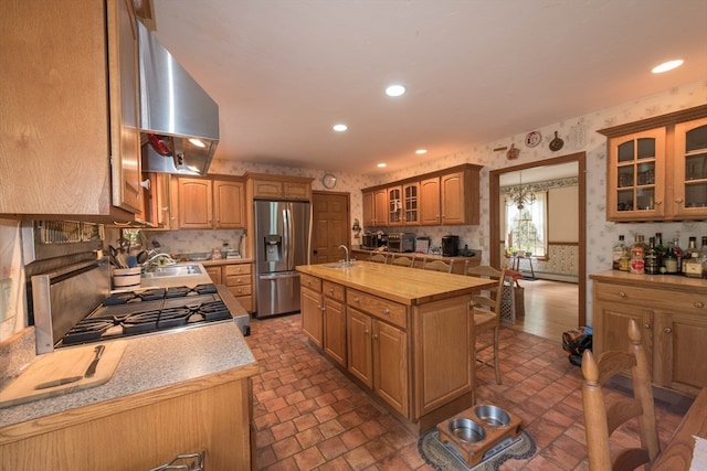 kitchen with a kitchen breakfast bar, stainless steel appliances, range hood, a kitchen island with sink, and sink