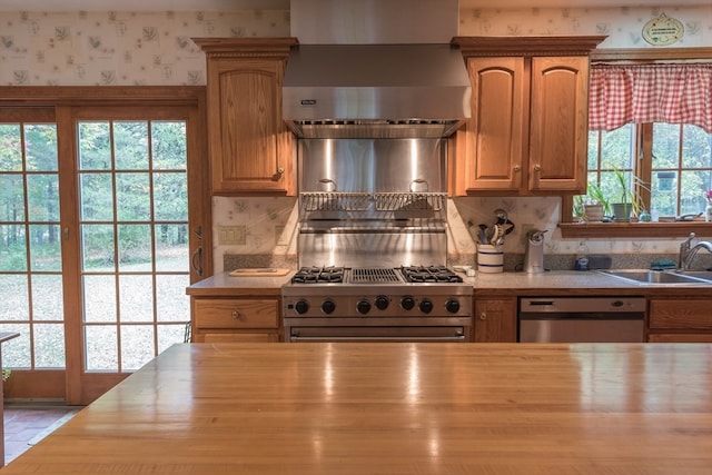 kitchen featuring butcher block counters, appliances with stainless steel finishes, wall chimney range hood, and sink