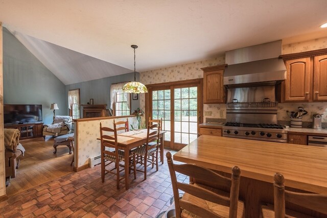 kitchen featuring lofted ceiling, hanging light fixtures, wall chimney exhaust hood, stainless steel range, and decorative backsplash