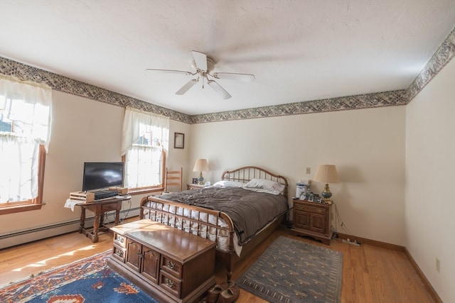 bedroom featuring multiple windows, a baseboard heating unit, hardwood / wood-style floors, and ceiling fan