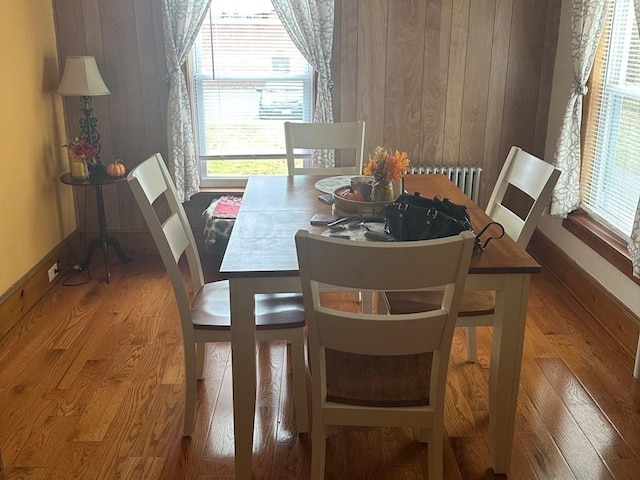 dining space with wood walls, wood-type flooring, and radiator heating unit