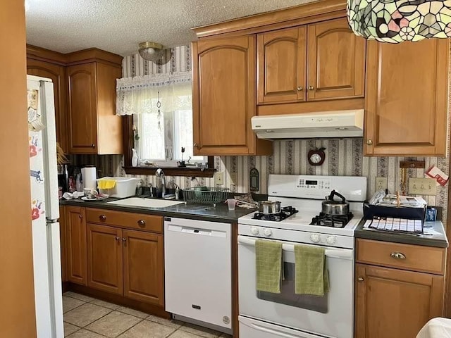 kitchen featuring white appliances, wallpapered walls, under cabinet range hood, and a sink