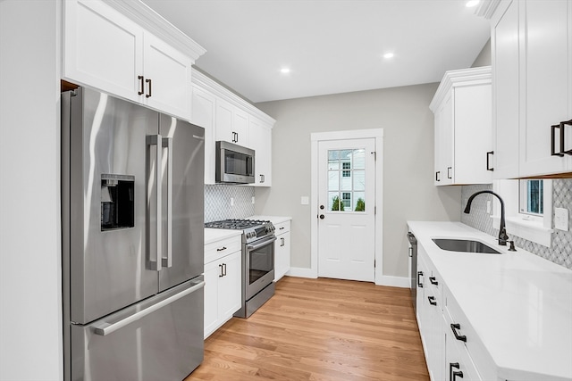 kitchen featuring backsplash, white cabinets, sink, light hardwood / wood-style floors, and stainless steel appliances