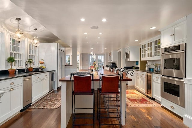 kitchen with glass insert cabinets, dark countertops, appliances with stainless steel finishes, dark wood finished floors, and beverage cooler