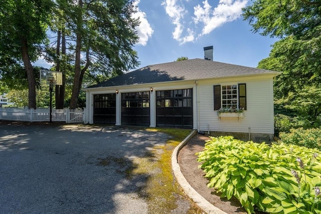 exterior space with a shingled roof, a garage, and fence
