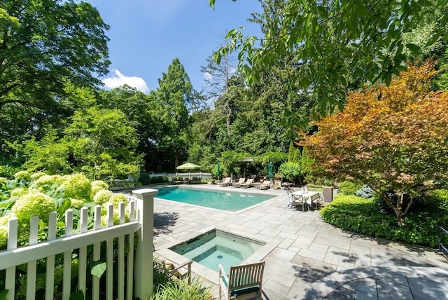 pool with a patio area, fence, and an in ground hot tub