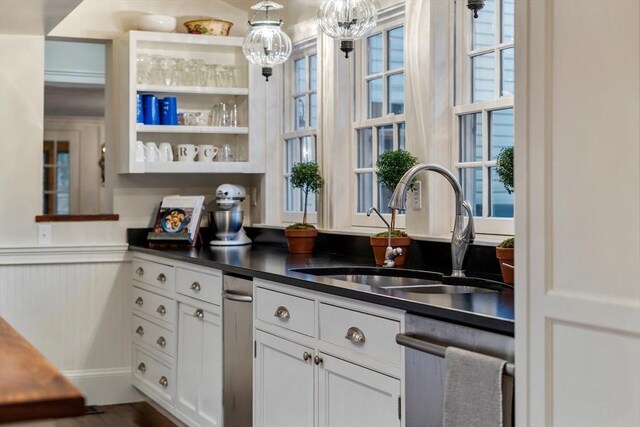 bar featuring hanging light fixtures, baseboards, dishwasher, a sink, and wood finished floors