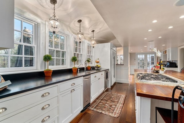 kitchen featuring dark wood-type flooring, white cabinets, appliances with stainless steel finishes, a sink, and hanging light fixtures