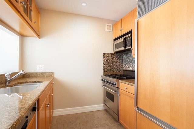 kitchen featuring a sink, stone countertops, baseboards, high end appliances, and backsplash