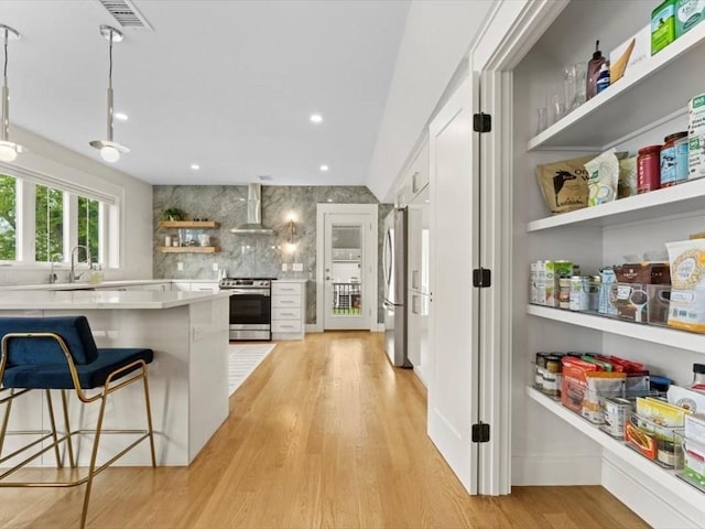 39 Paul St, Watertown, MA 02472 - kitchen with open shelves, stainless steel appliances, wall chimney range hood, light wood finished floors, and light countertops