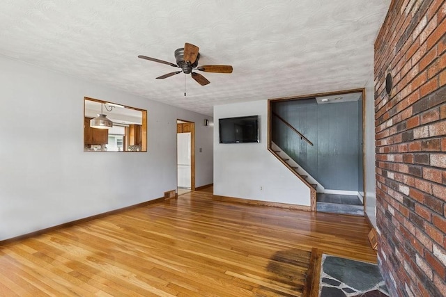 32 Cambo St, Brockton, MA 02301 - unfurnished living room with wood finished floors, ceiling fan, stairs, a textured ceiling, and brick wall