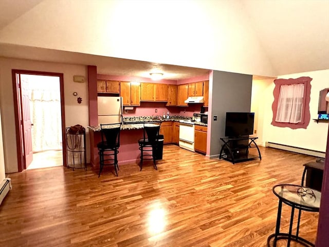 kitchen with a breakfast bar area, vaulted ceiling, light wood-type flooring, a baseboard radiator, and white appliances